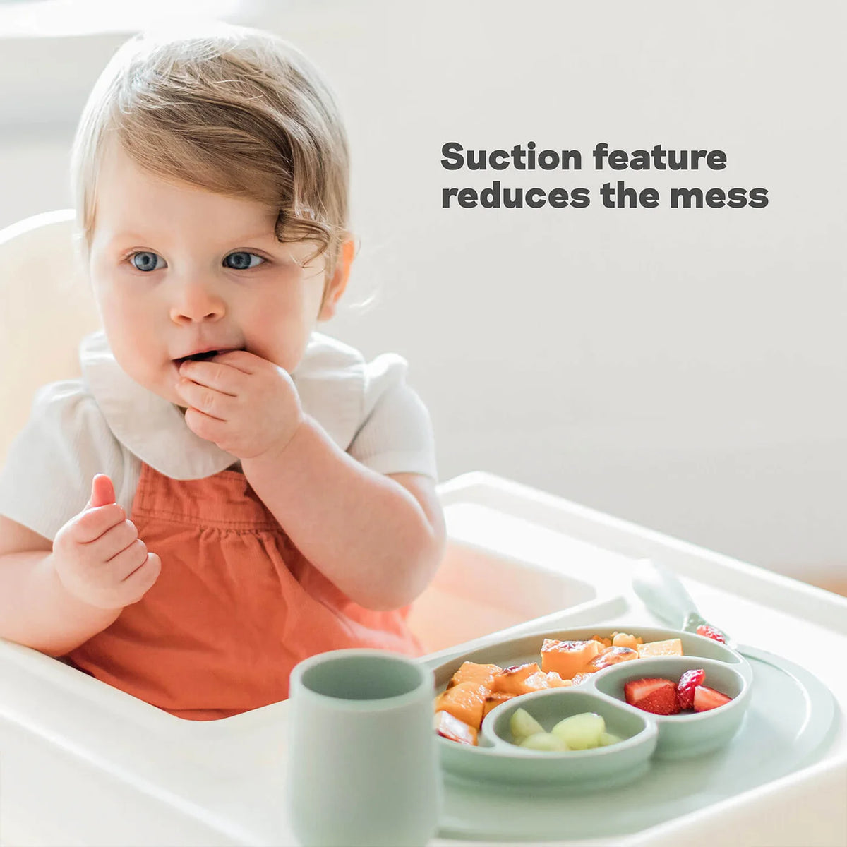 Child in a high chair with a tray of food and text 'Suction feature reduces the mess'.